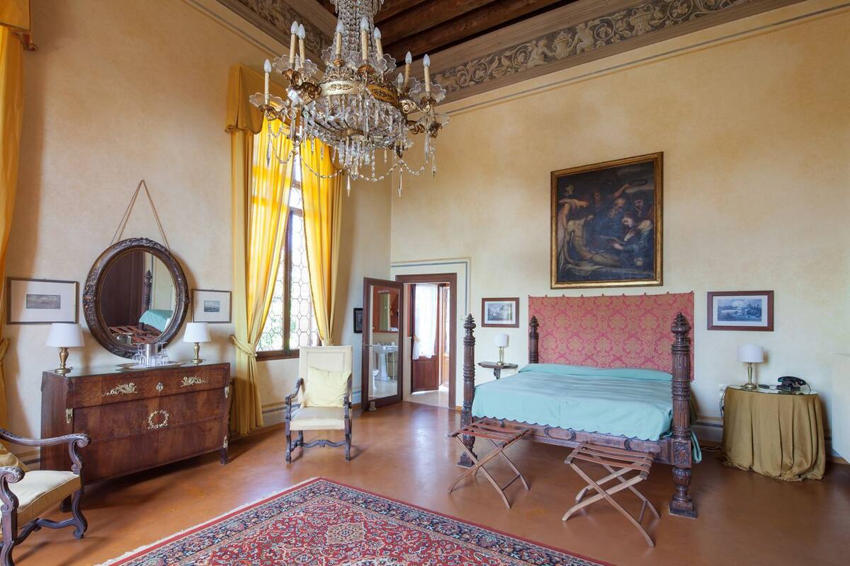 Un dormitorio espacioso con una cama grande, un candelabro, un aparador de madera, una silla y un cuadro en la pared.