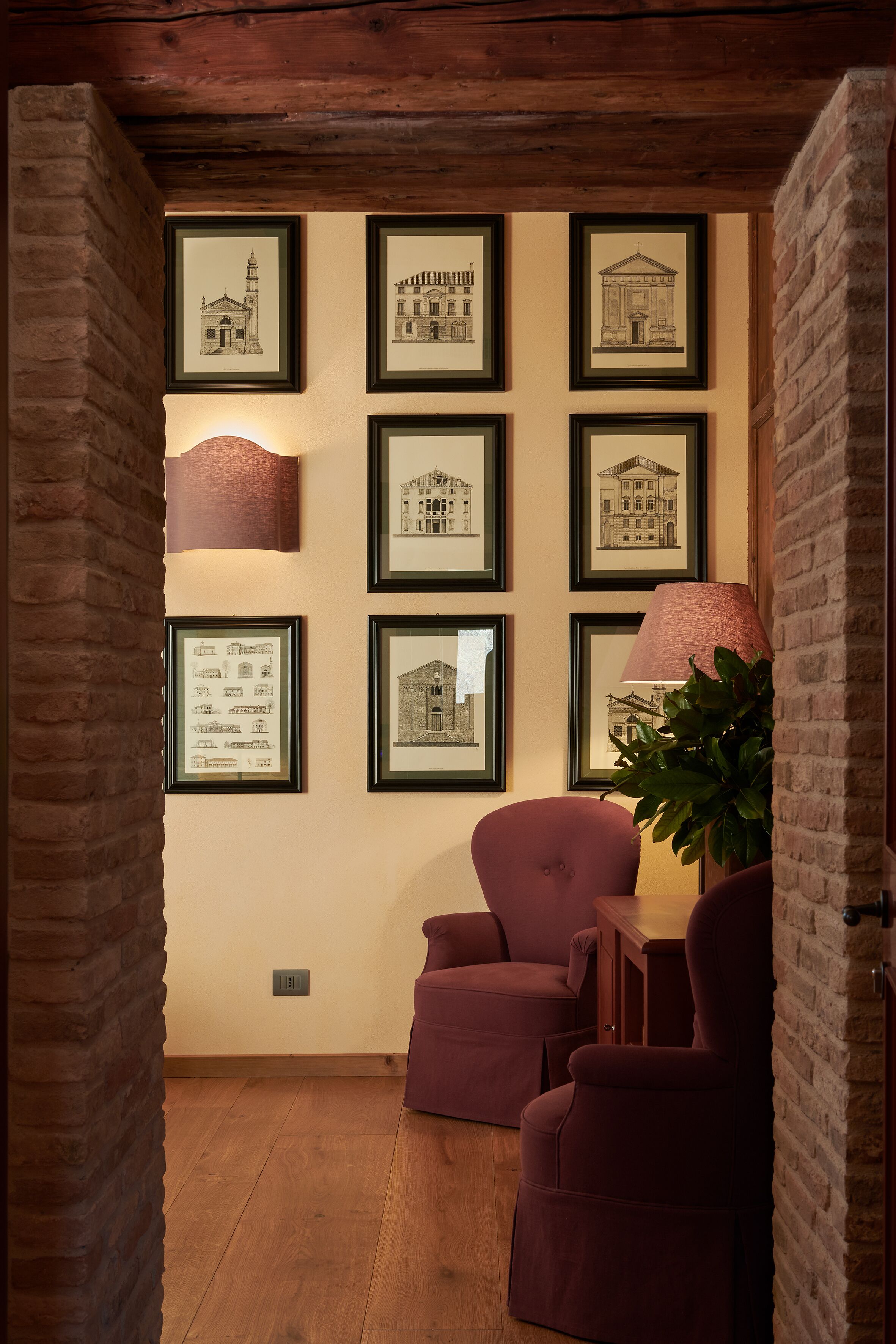 Una habitación con dibujos arquitectónicos enmarcados en la pared, suelo de madera y un sillón morado.