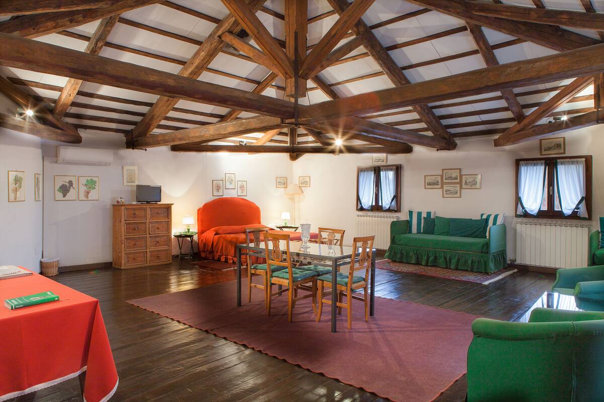 Una habitación amplia con un alto techo de madera, una mesa de comedor con sillas, un sofá y un sillón verde.