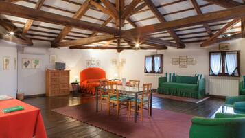 A spacious room with a high wooden ceiling, a dining table with chairs, a sofa, and a green armchair.