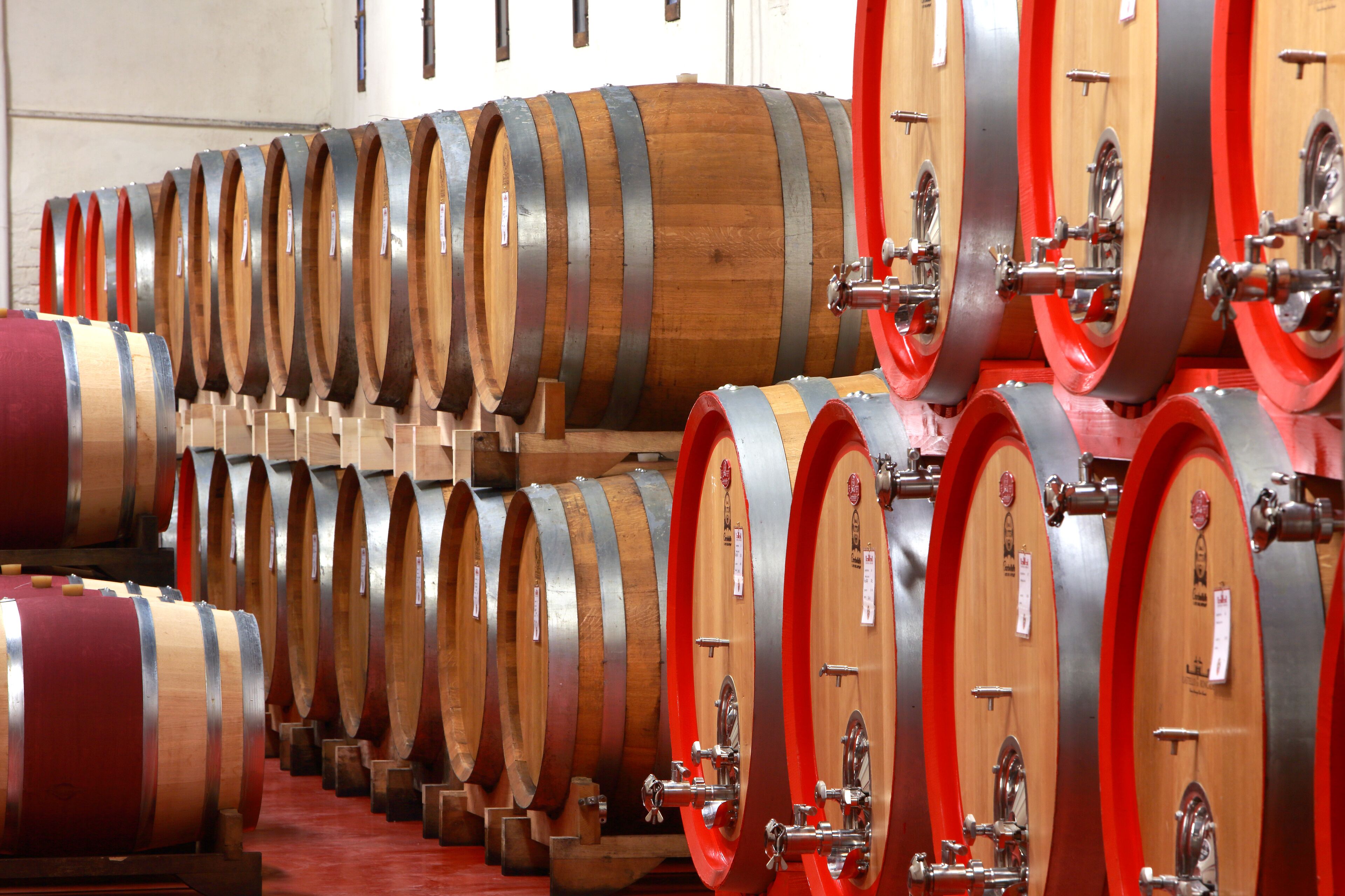 Rows of wooden wine barrels with metal hoops and red accents, likely in a storage or aging facility.