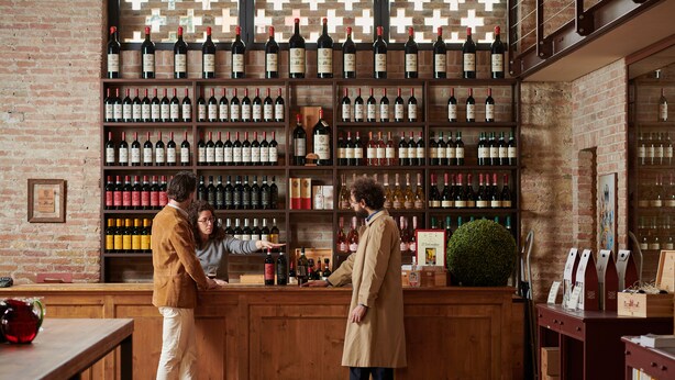 Zona de bar con estantes de madera llenos de botellas de vino, una barra y una pared de ladrillo.