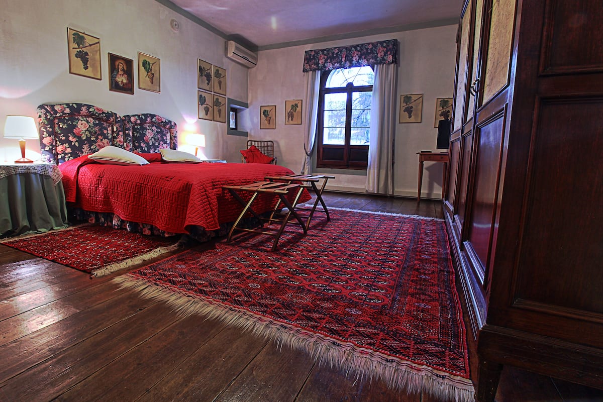 Una habitación tradicional con piso de madera, colcha roja y una alfombra grande de color rojo.