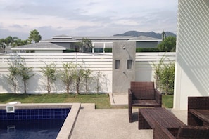 Un área de piscina con sillas de descanso y una piscina pequeña, rodeada por un muro blanco y vegetación.