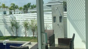 A glass door leading to an outdoor patio with wicker furniture and a swimming pool. - Baan Sarinya Pool Villa (Cha-am)