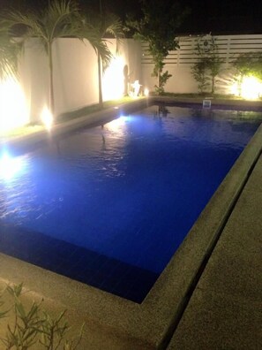 En swimmingpool med blå kakel på insidan, omgiven av en låg mur och palmer.
