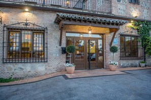 A brick building with a wooden entrance, large windows with metal bars, and potted plants. - Hotel Los Cigarrales (Toledo)