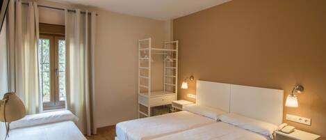 Habitación de hotel con dos camas, un escritorio con lámpara, un armario y una ventana con cortinas.