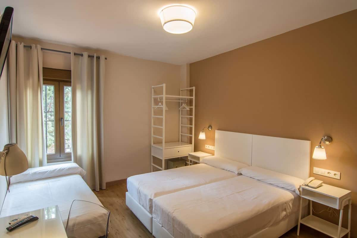 Habitación de hotel con dos camas, un escritorio, una silla, un televisor, un armario y una ventana con cortinas.