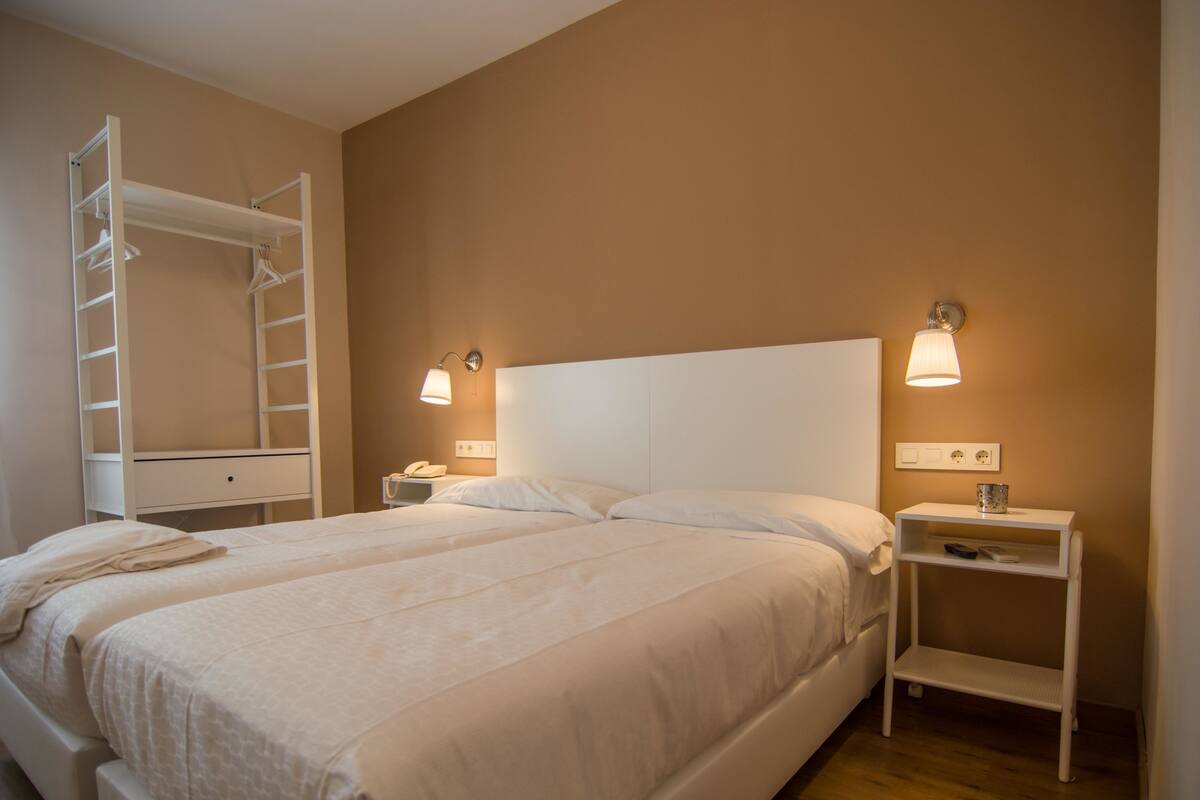 Un dormitorio con cama, mesita de noche, lámpara, armario y estante.