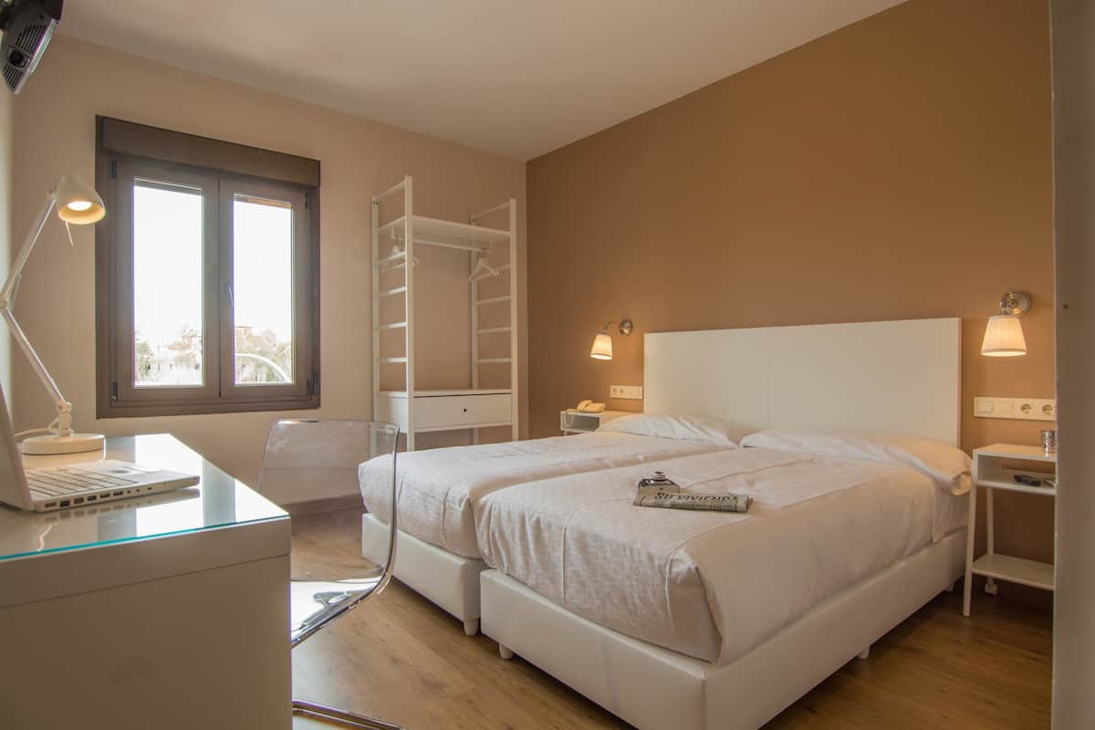 Un dormitorio con dos camas, un escritorio con una computadora portátil, una silla, una escalera y lámparas de noche.