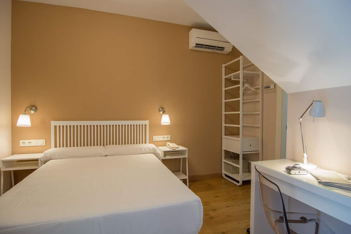 Un dormitorio con cama, mesitas de noche, escritorio, silla, armario y equipo de aire acondicionado.