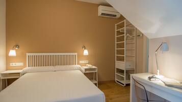 Un dormitorio con cama, mesitas de noche, escritorio, silla, armario y equipo de aire acondicionado.
