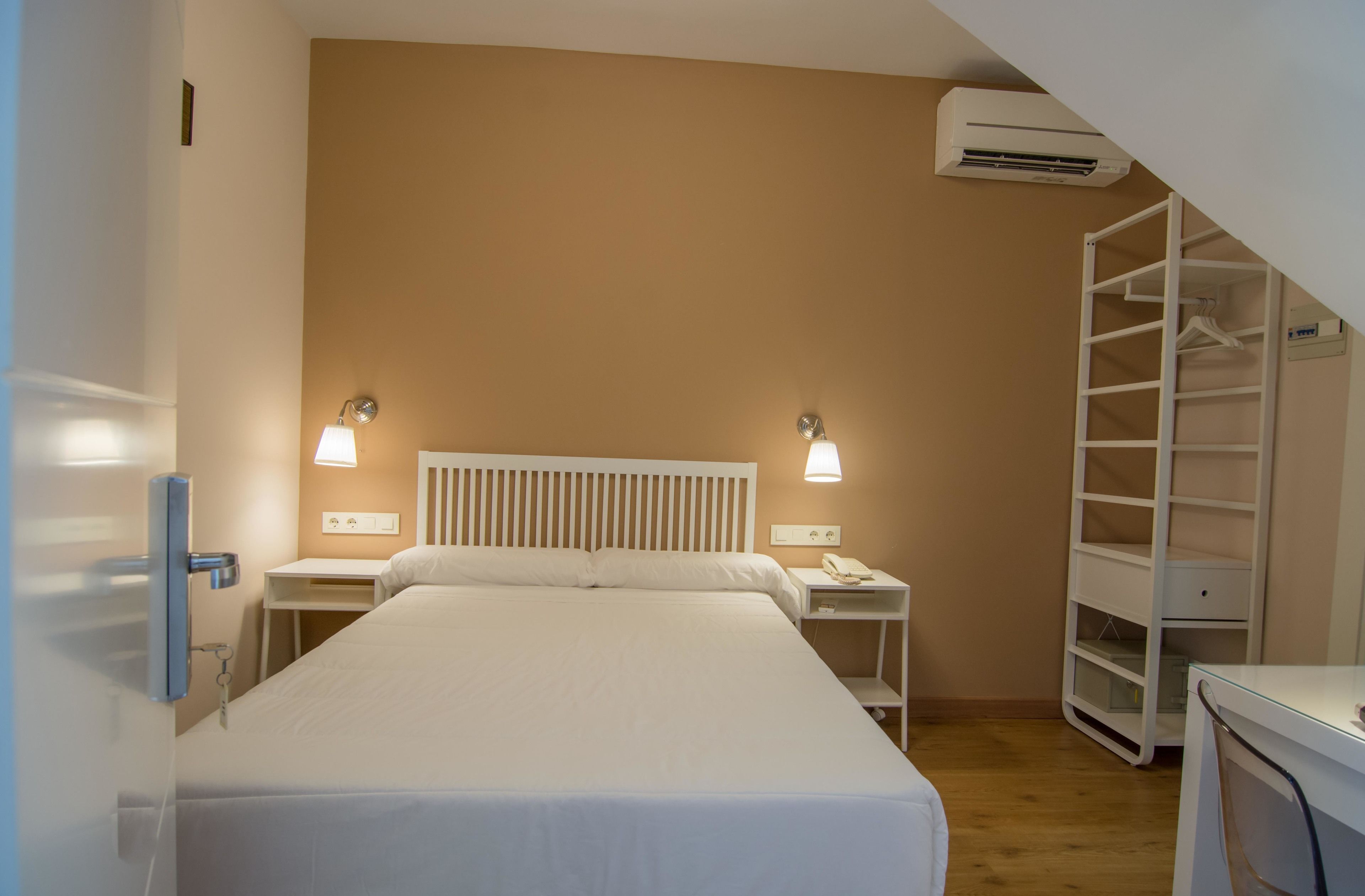 Una habitación de hotel con cama, mesitas de noche, lámpara, aire acondicionado y armario.