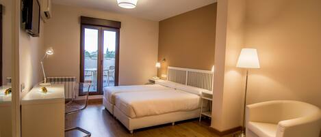 A hotel room with a bed, two bedside tables, a chair, a desk, and a radiator.
