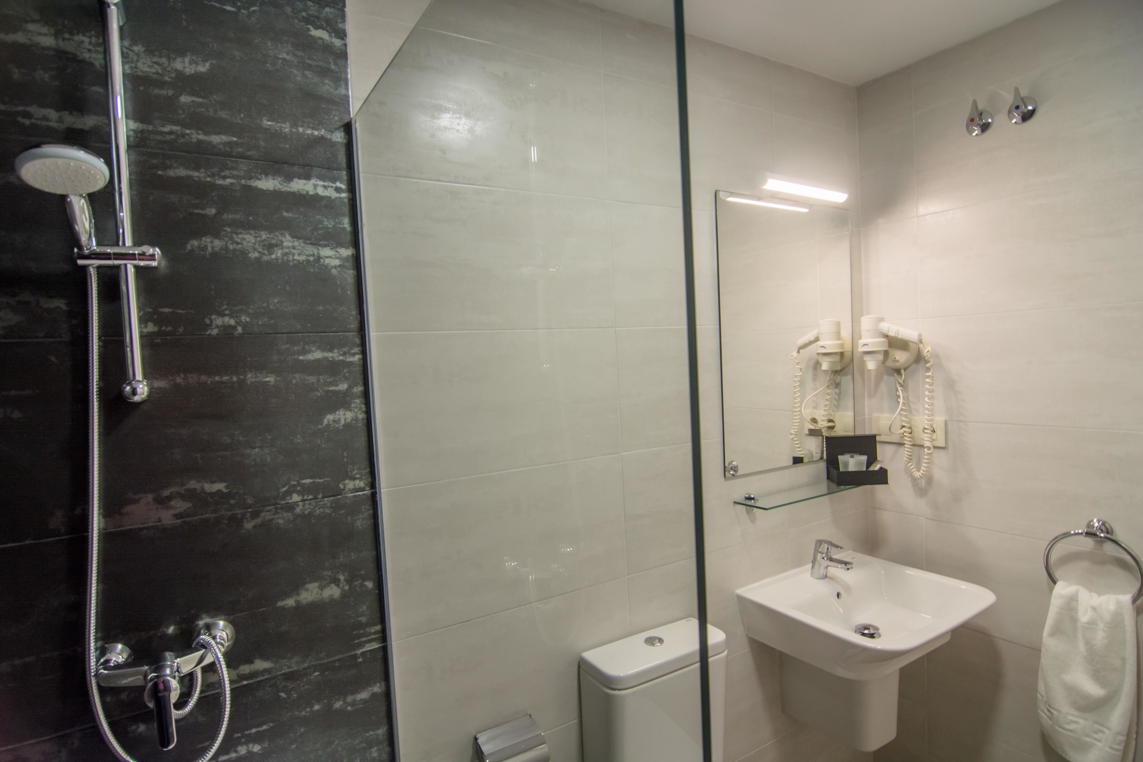 Un baño moderno con ducha envuelta en vidrio, lavamanos blanco y retrete.