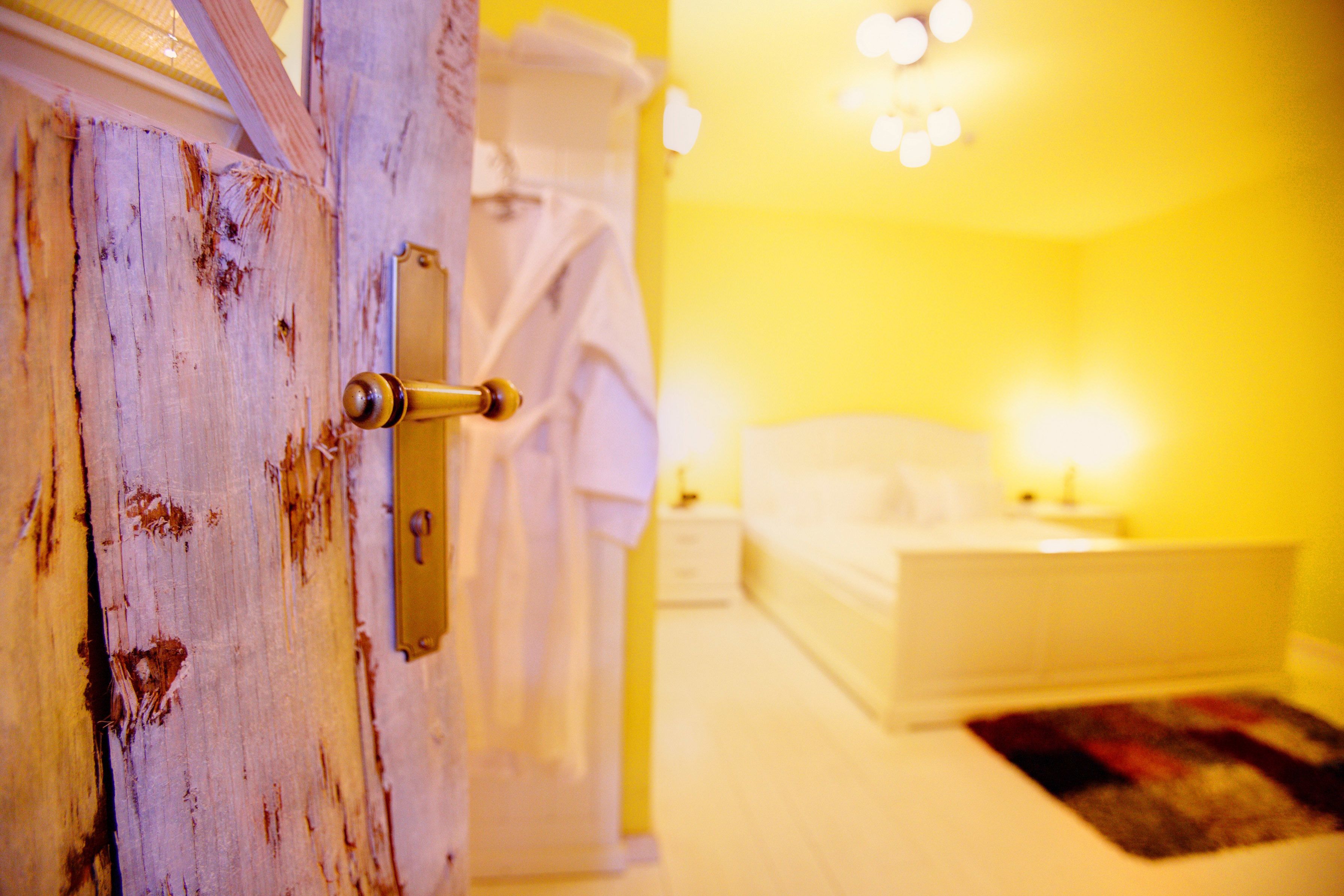 A room with a wooden door, a white bed, and a nightstand with a lamp.