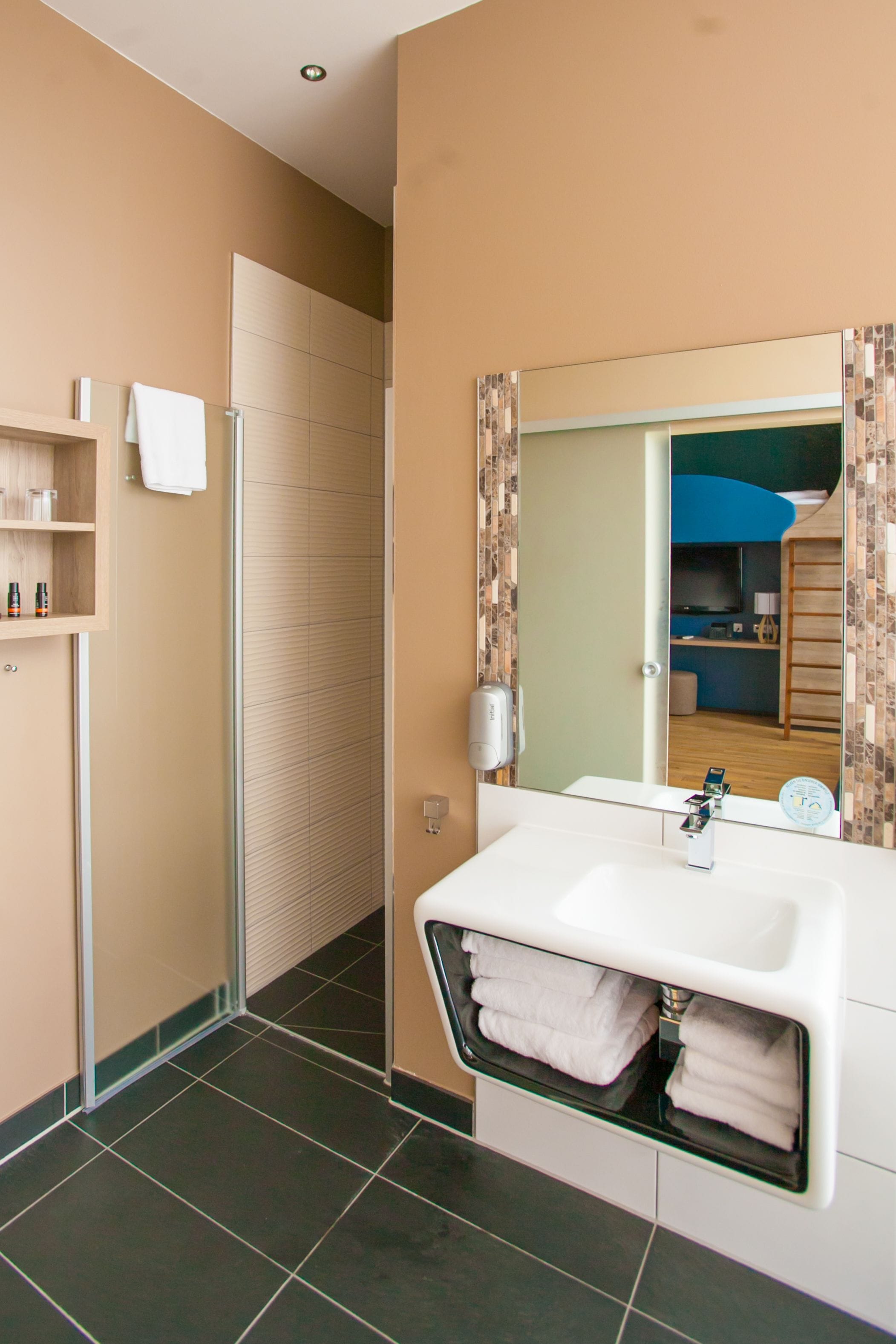 Un baño moderno con un lavabo blanco, cabina de ducha de vidrio y espejo con marco decorativo.
