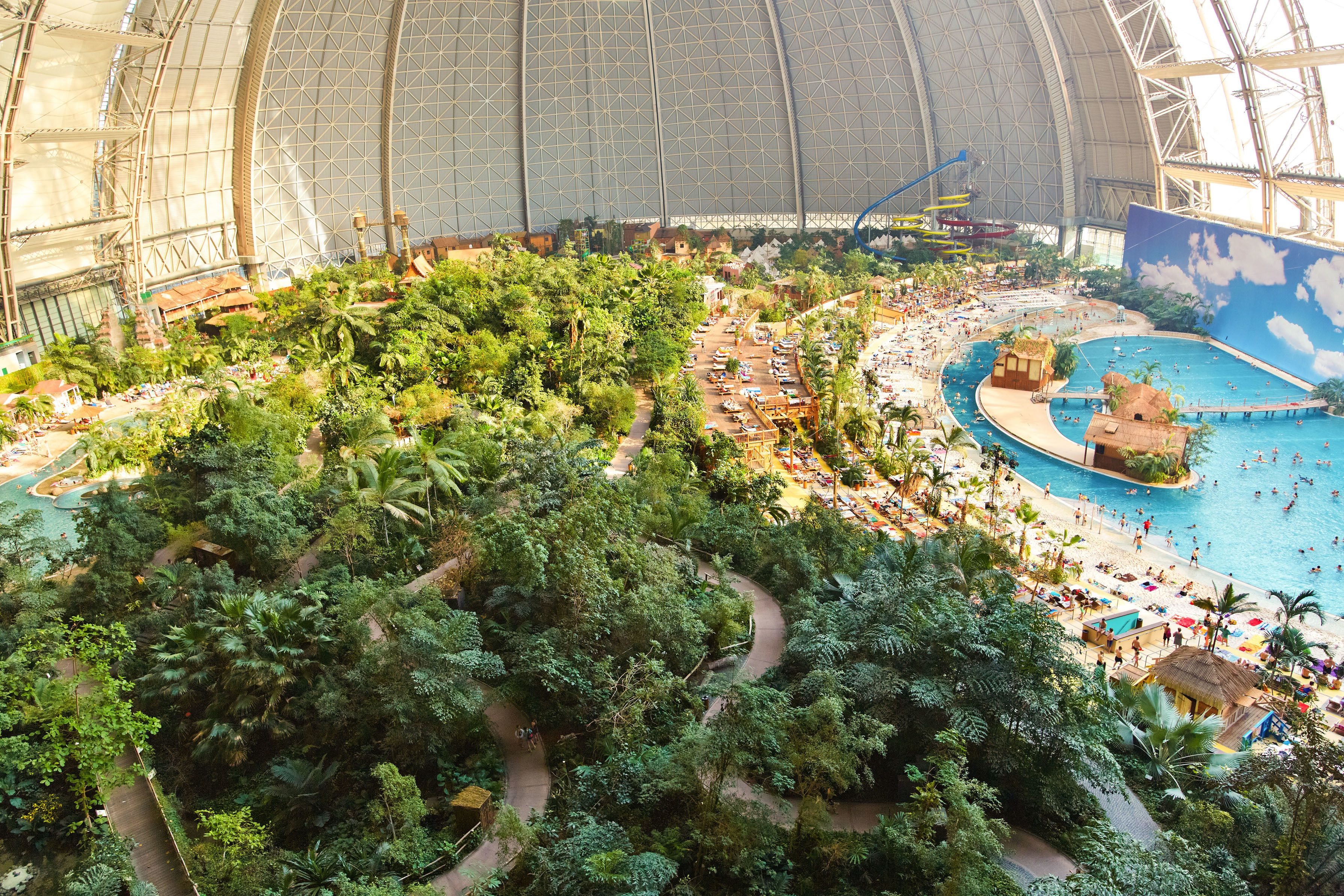 An indoor theme park with a large dome structure, a central pool area, and lush greenery.