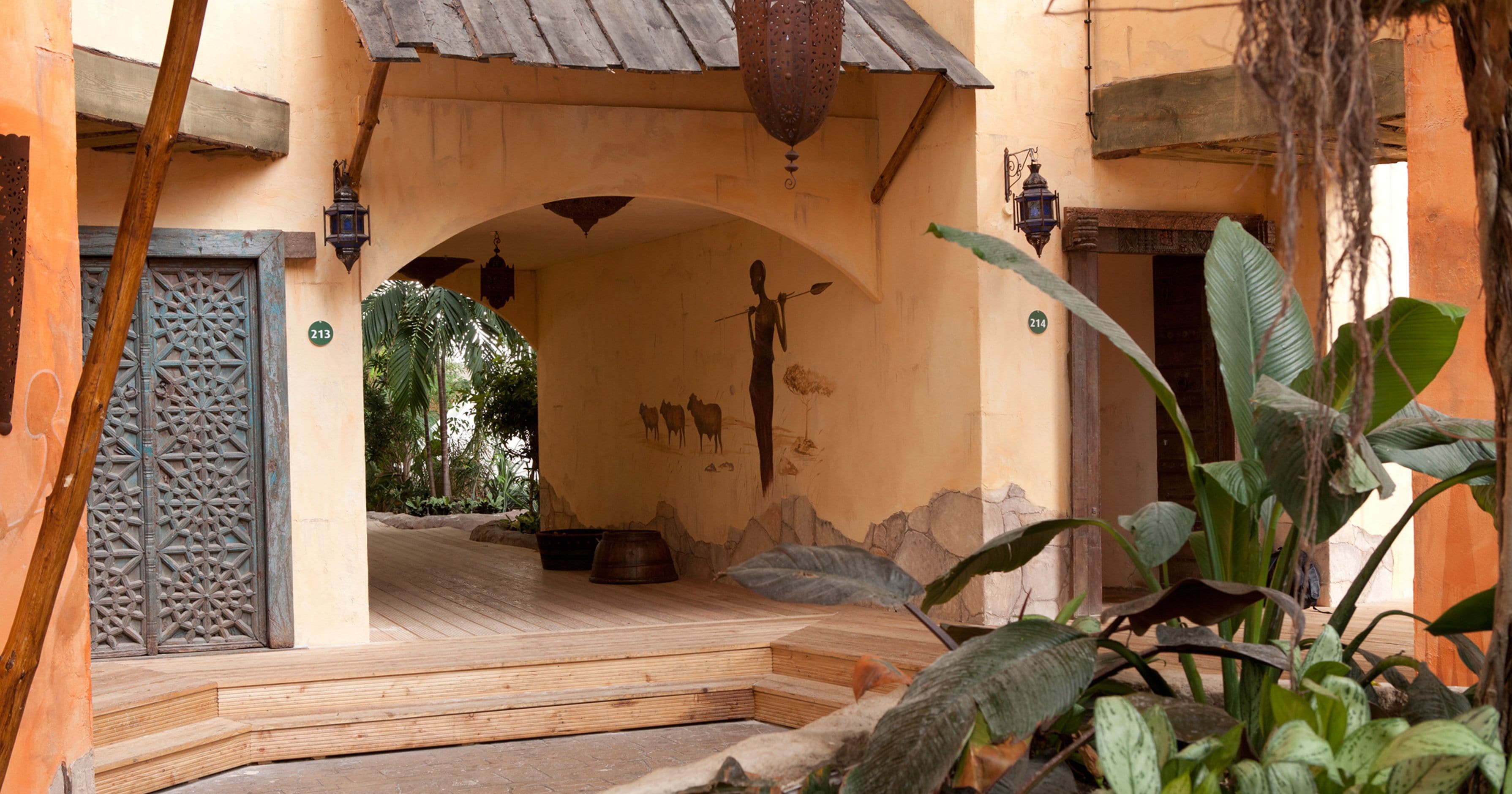 A traditional Moroccan interior with a wooden door, a decorative archway, and a view of the courtyard.