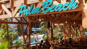 Een houten constructie met het bord 'Palm Beach', wat duidt op een resort of hotel.