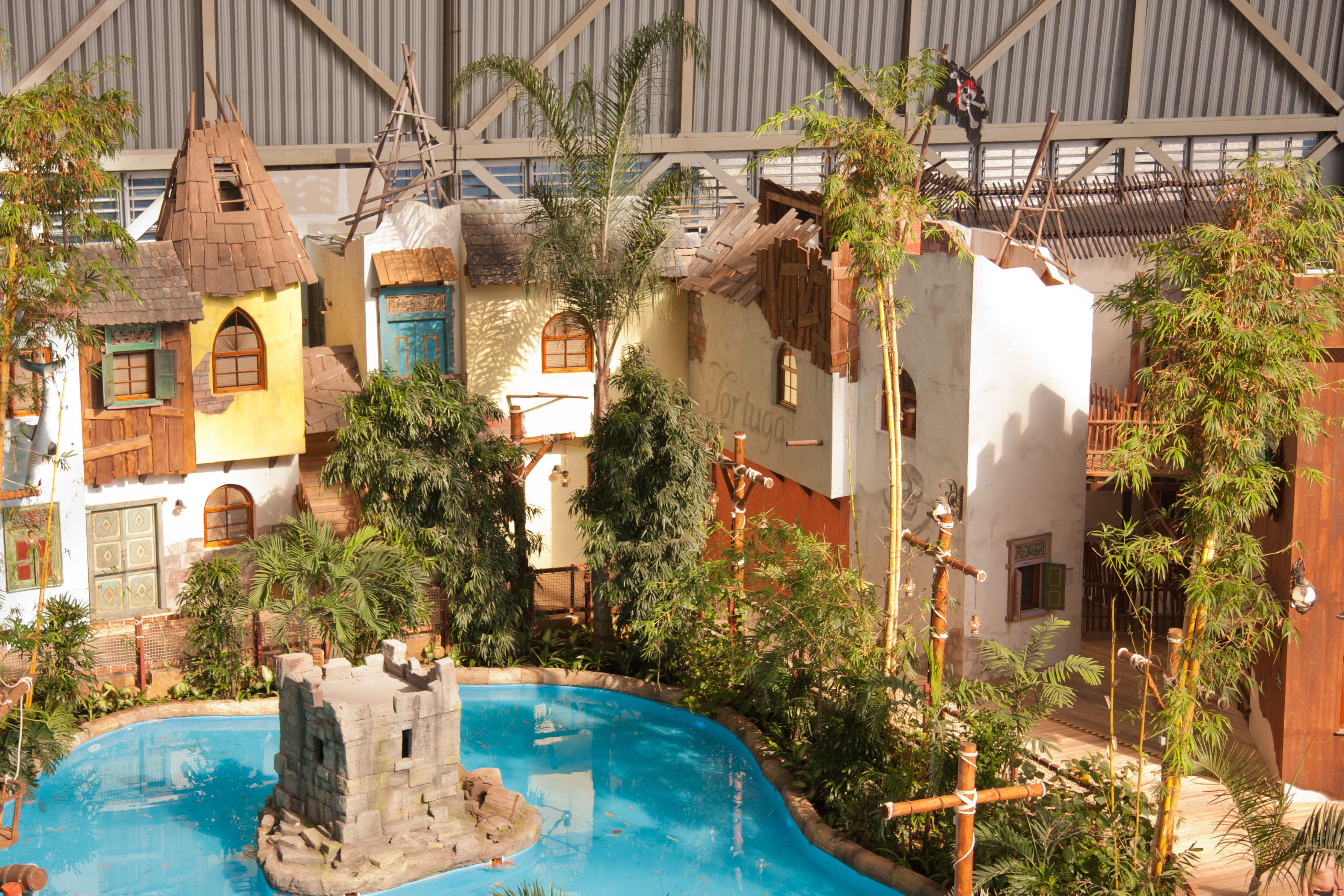 A pool area with a castle-like structure, surrounded by tropical plants and buildings with unique architectural styles.