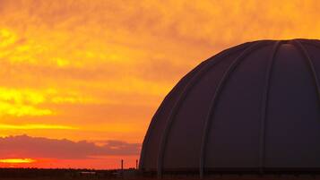 Ein großes, kuppelartiges Gebäude mit flachem Dach, eingebettet in eine flache Landschaft mit Sonnenuntergang im Hintergrund.