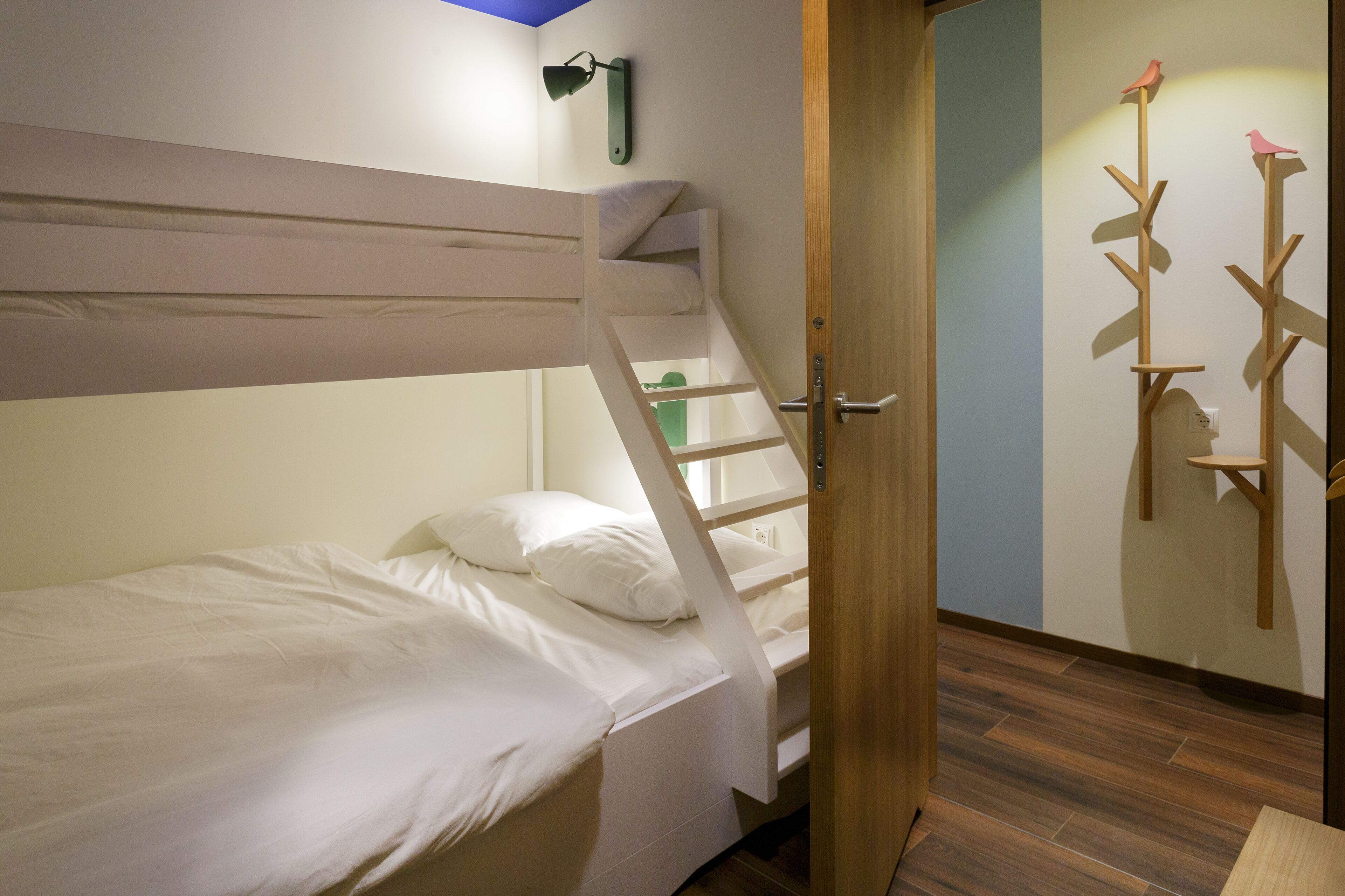 Ein Stockbett mit einer Leiter, eine Holztür und ein an der Wand befestigtes Regal mit einer Vogeldekoration.