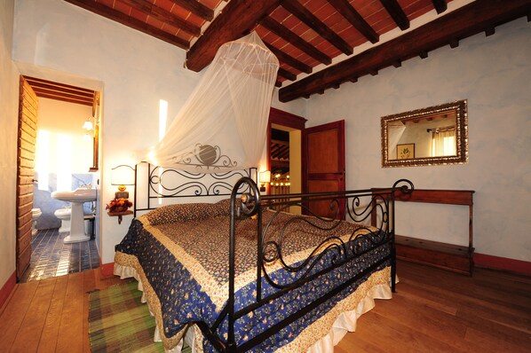 Un dormitorio con cama, mesita de noche, espejo y ventana con cortina.