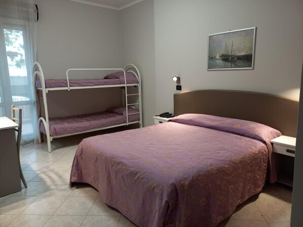 A room with bunk beds, a desk, a chair, a bedside table, a lamp, and a painting on the wall. - Susy (Rimini)
