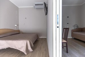 A bedroom with a bed, a chair, a sofa, and an air conditioning unit. - Susy (Rimini)