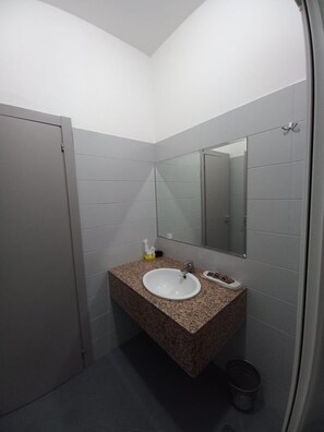 A bathroom with a granite countertop sink, a mirror, a towel dispenser, and a trash bin. - Susy (Rimini)