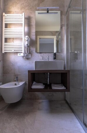 A modern bathroom with a bidet, a sink, a mirror, and a shower enclosure. - Susy (Rimini)