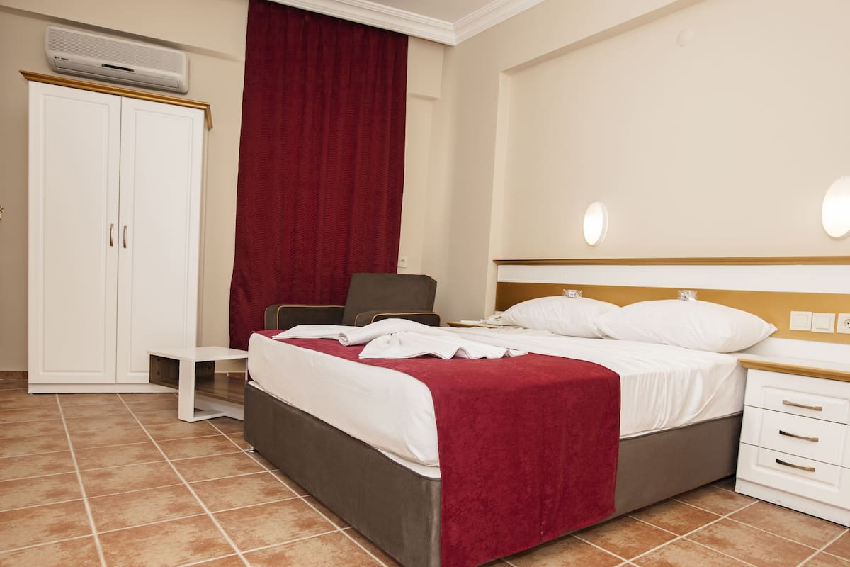 A hotel room with a bed, bedside tables, a wardrobe, and an air conditioning unit.