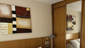 A neatly made bed with white and blue bedding, a wooden headboard, a wall-mounted artwork, and a mirror reflecting the room. - Hotel Villa de Llanes (Llanes)