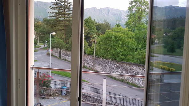 A view from a window overlooking a road with a stone wall, a street lamp, and a mountain range in the background. - Hotel Villa de Llanes (Llanes)