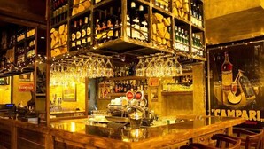 A bar area with shelves of bottles, a bar counter, and hanging glasses. - Marmore (Cervinia)
