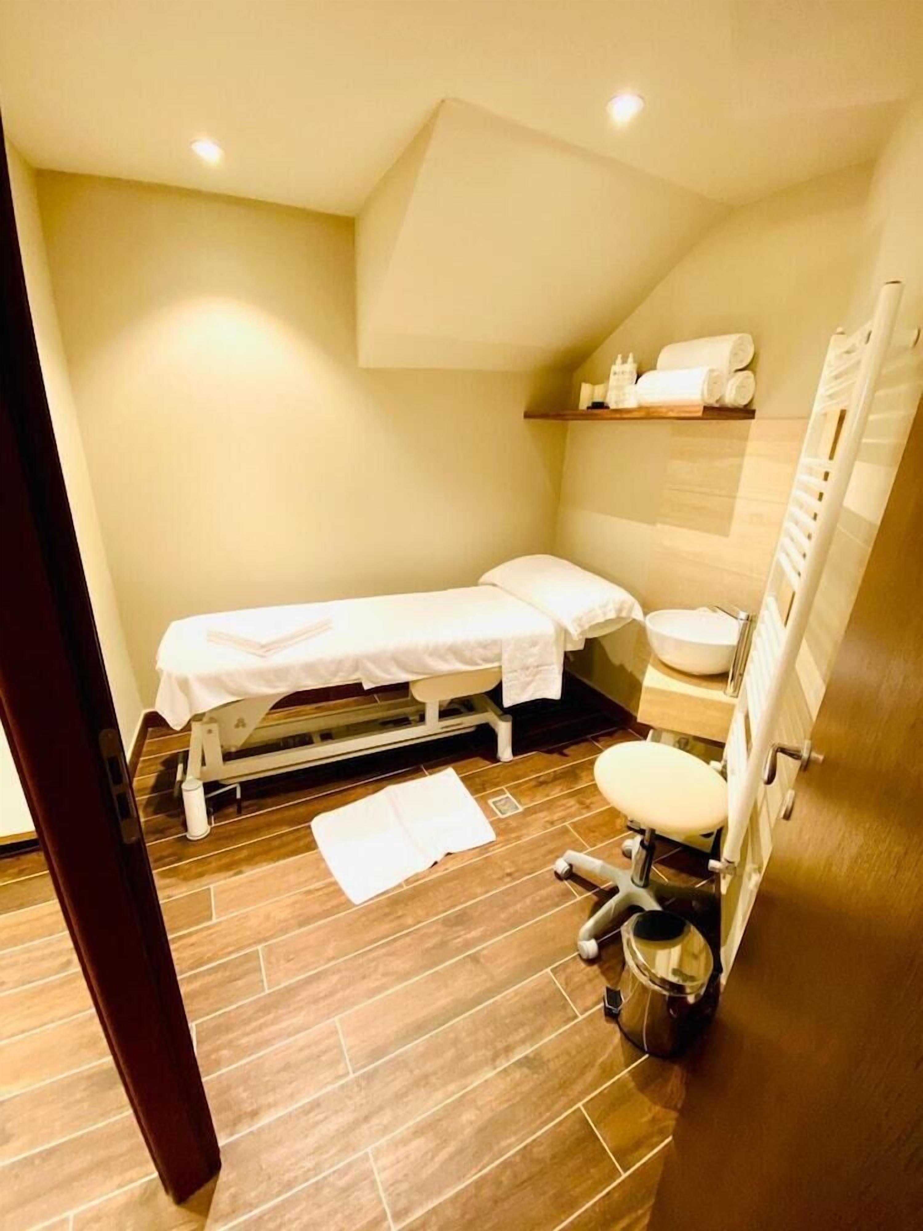 Una piccola struttura sanitaria con un'unica stanza, dotata di pavimento in legno, un letto, un lavandino e un water.