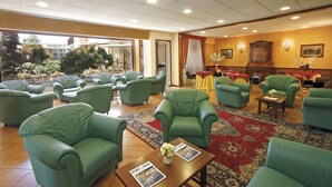 A hotel lobby with green armchairs, a red patterned rug, and a view of the outdoors. - Hotel Mondial (Rapallo)