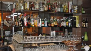 A bar with multiple shelves stocked with various liquor bottles and a large number of glasses arranged on the counter. - Hotel Mondial (Rapallo)