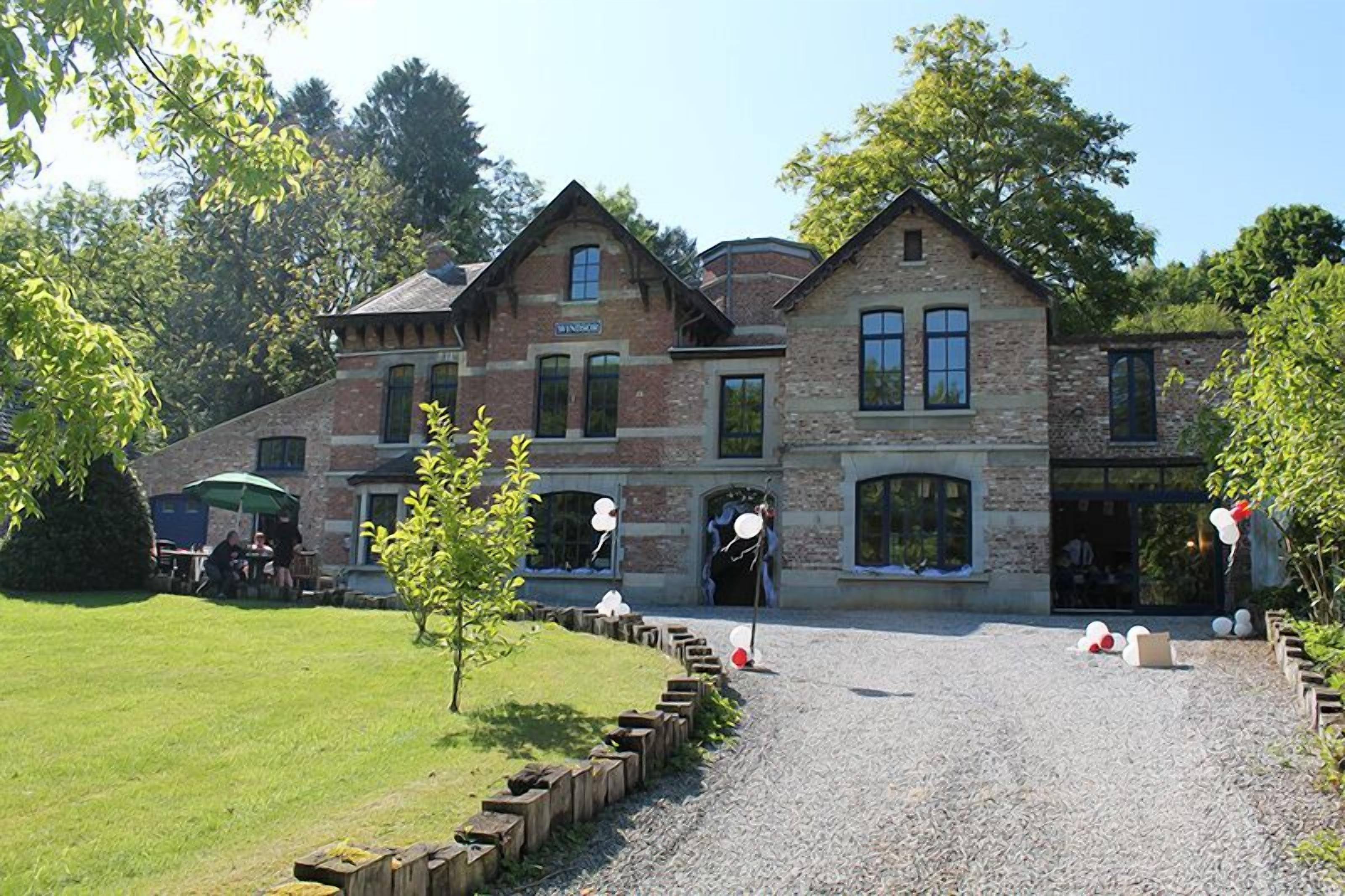 Un grand bâtiment en pierre à plusieurs étages, de style architectural traditionnel, avec une allée gravillonnée et une pelouse bien entretenue.