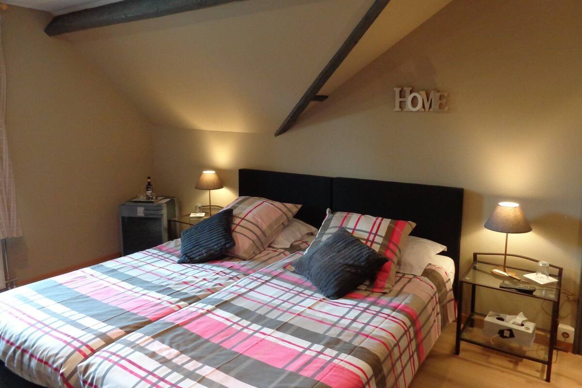 Une chambre à coucher avec un lit, deux tables de chevet, une lampe et un panneau indiquant « Chez nous » sur le mur.