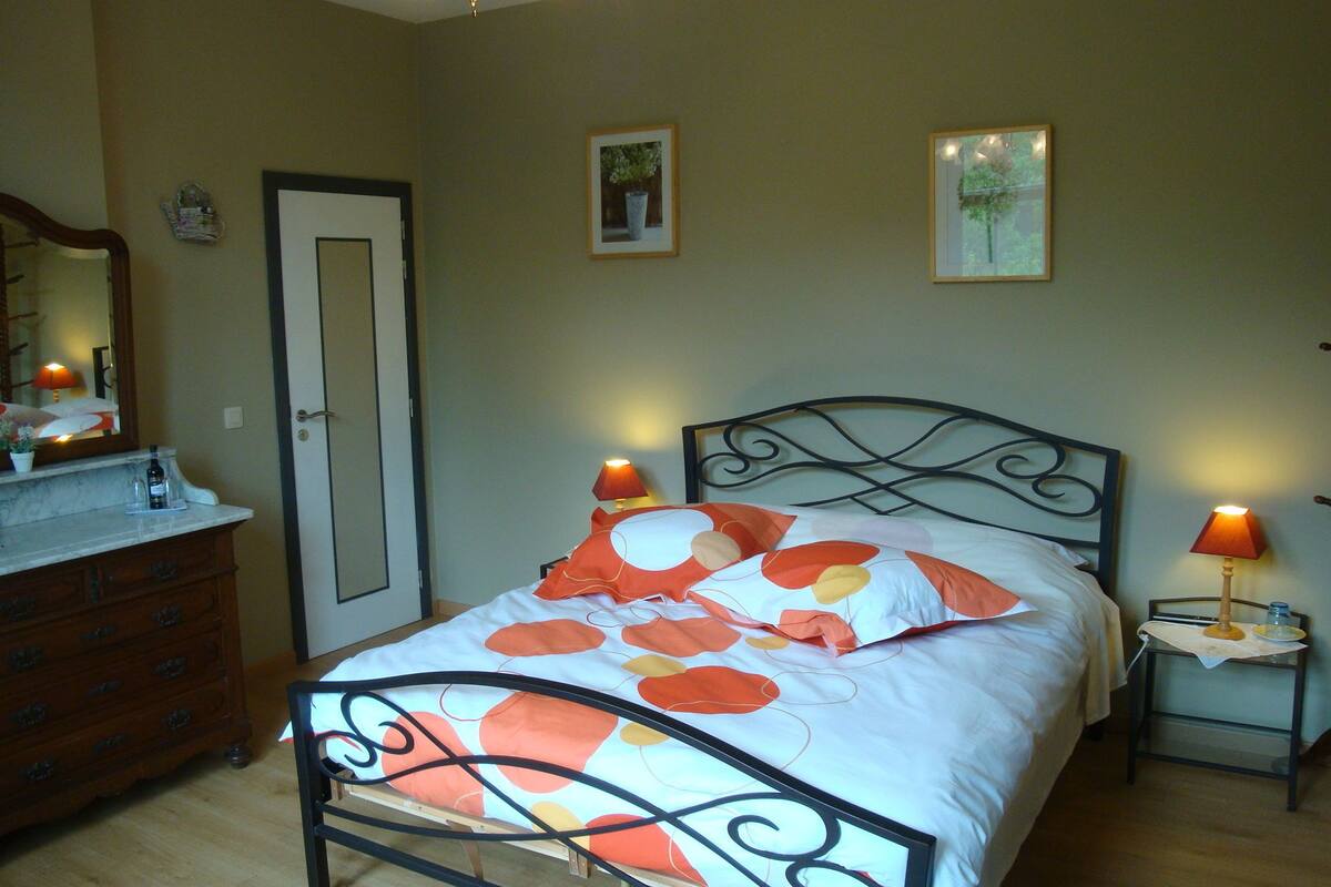Une chambre à coucher avec un lit, des tables de chevet, une commode, une porte et deux tableaux encadrés accrochés au mur.