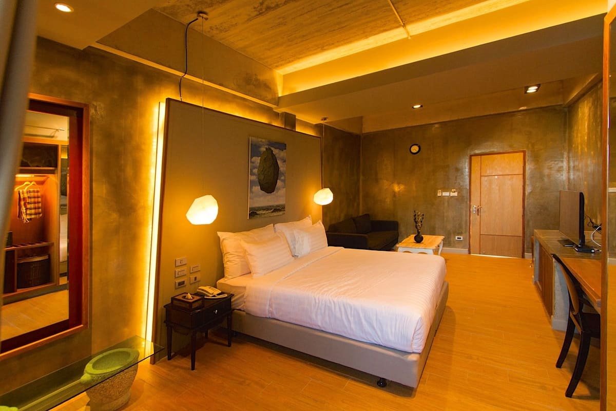 Une chambre d’hôtel moderne avec un grand lit, des lampes de chevet, un plancher en bois, un petit bureau et une armoire.