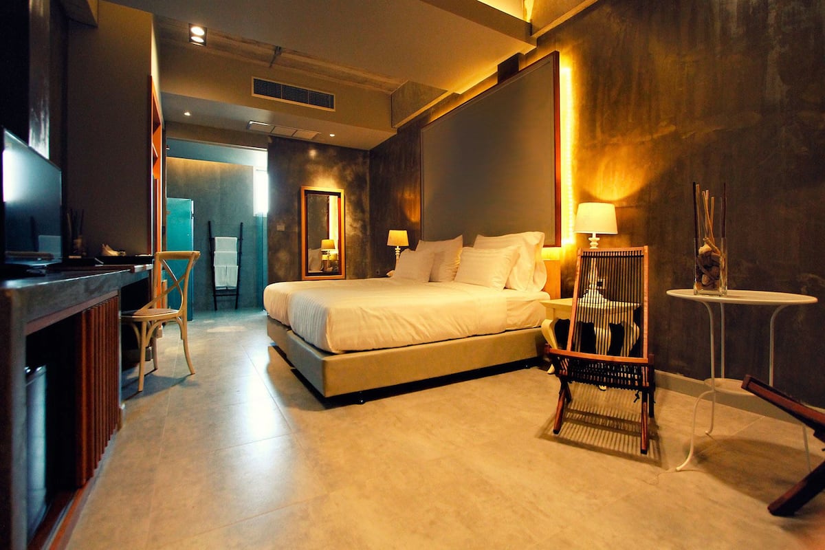 Une chambre d’hôtel moderne avec un grand lit, un bureau avec une chaise, une petite table avec une lampe et un miroir au mur.