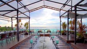 Een terras buiten met uitzicht op zee, met tafels en stoelen, een waterpartij en potplanten.