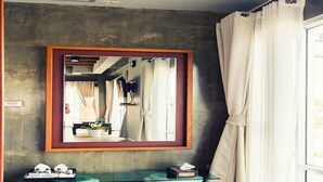 Een moderne badkamer met een grote spiegel, een bankje en een raam met gordijnen.
