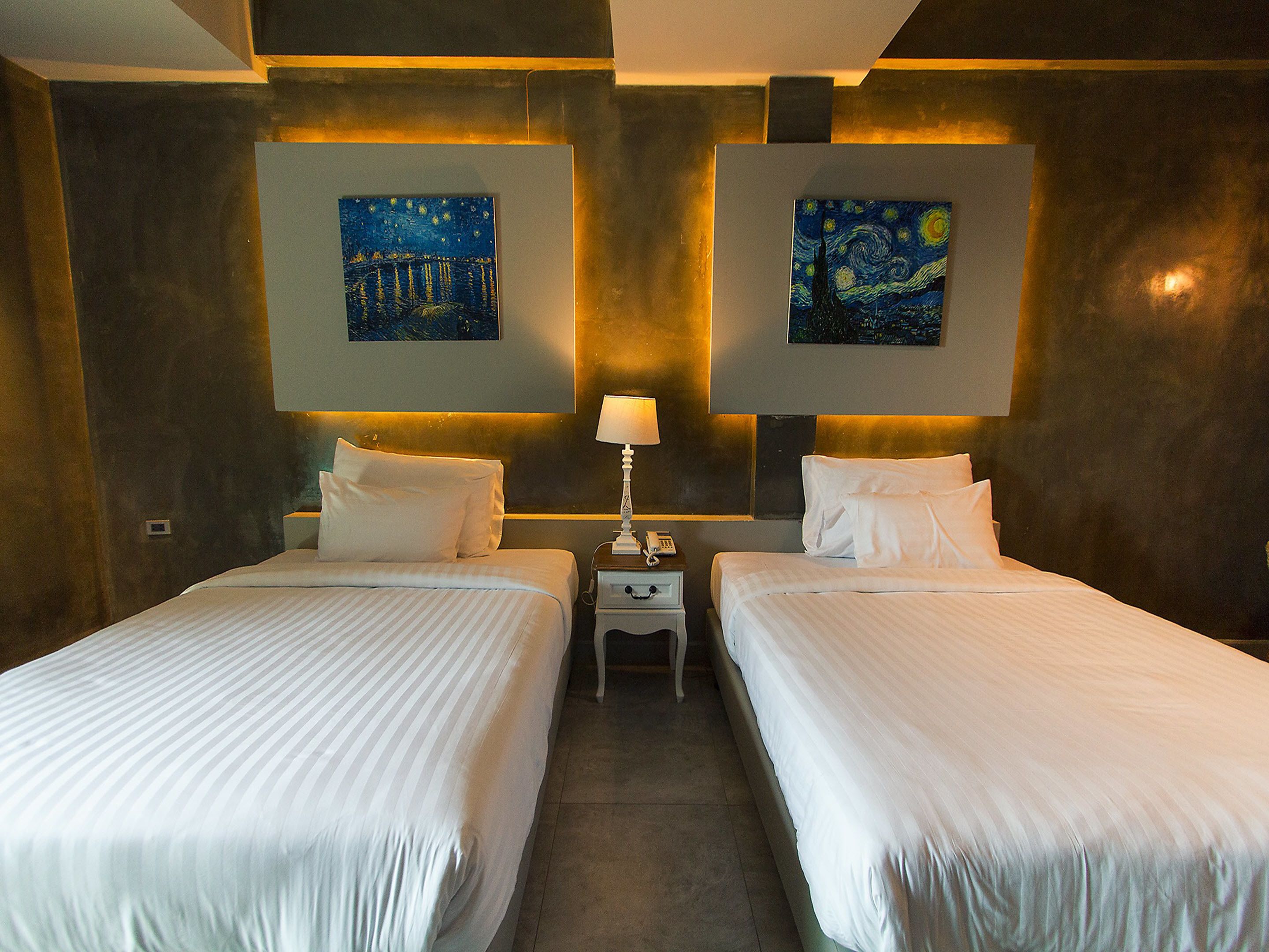 Une chambre d’hôtel avec deux lits, une table de chevet avec une lampe et deux tableaux accrochés aux murs.