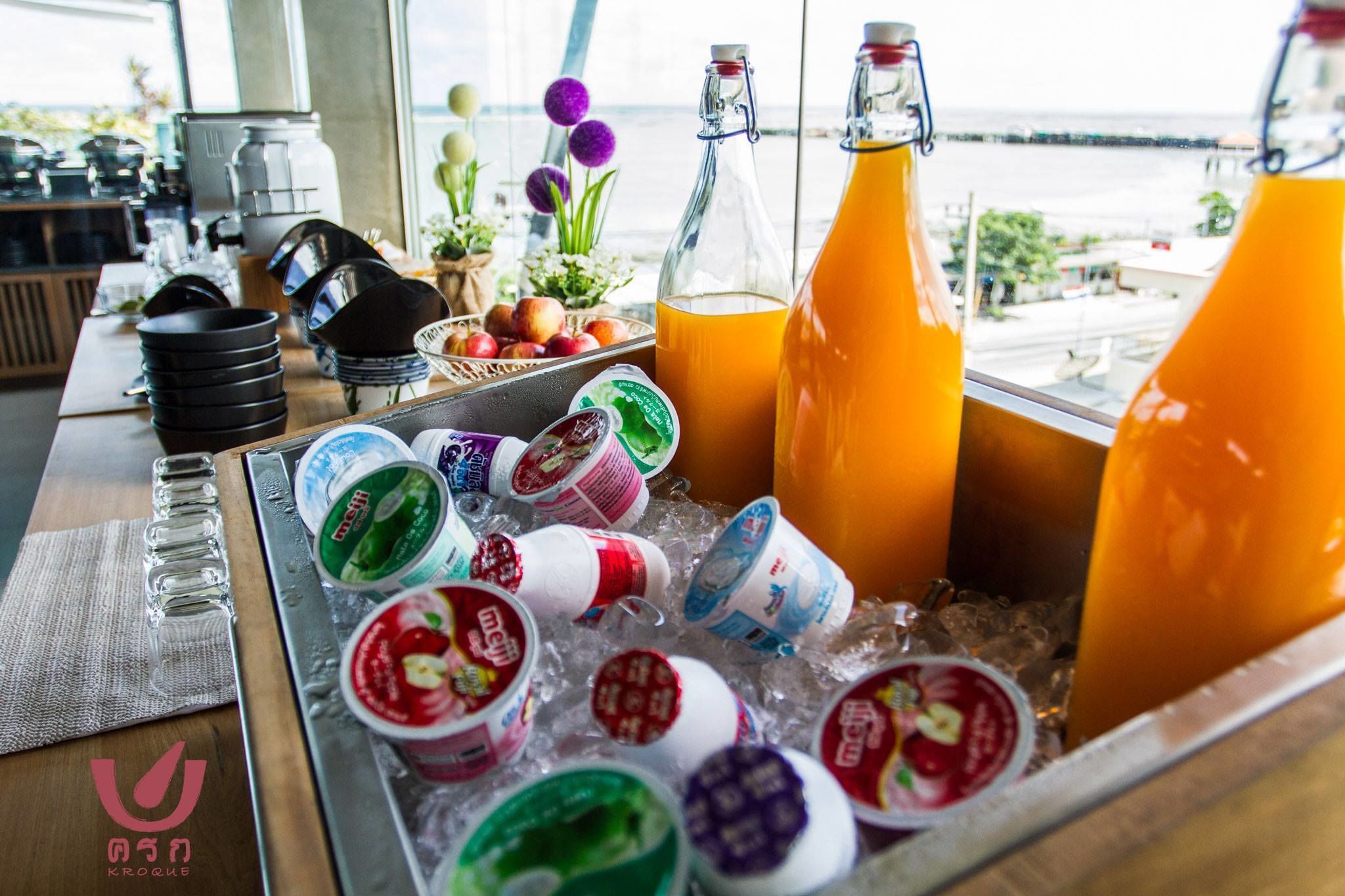 Uma área de bar com diversas bebidas, incluindo chá gelado e sucos, e uma seleção de potes de iogurte sobre gelo.