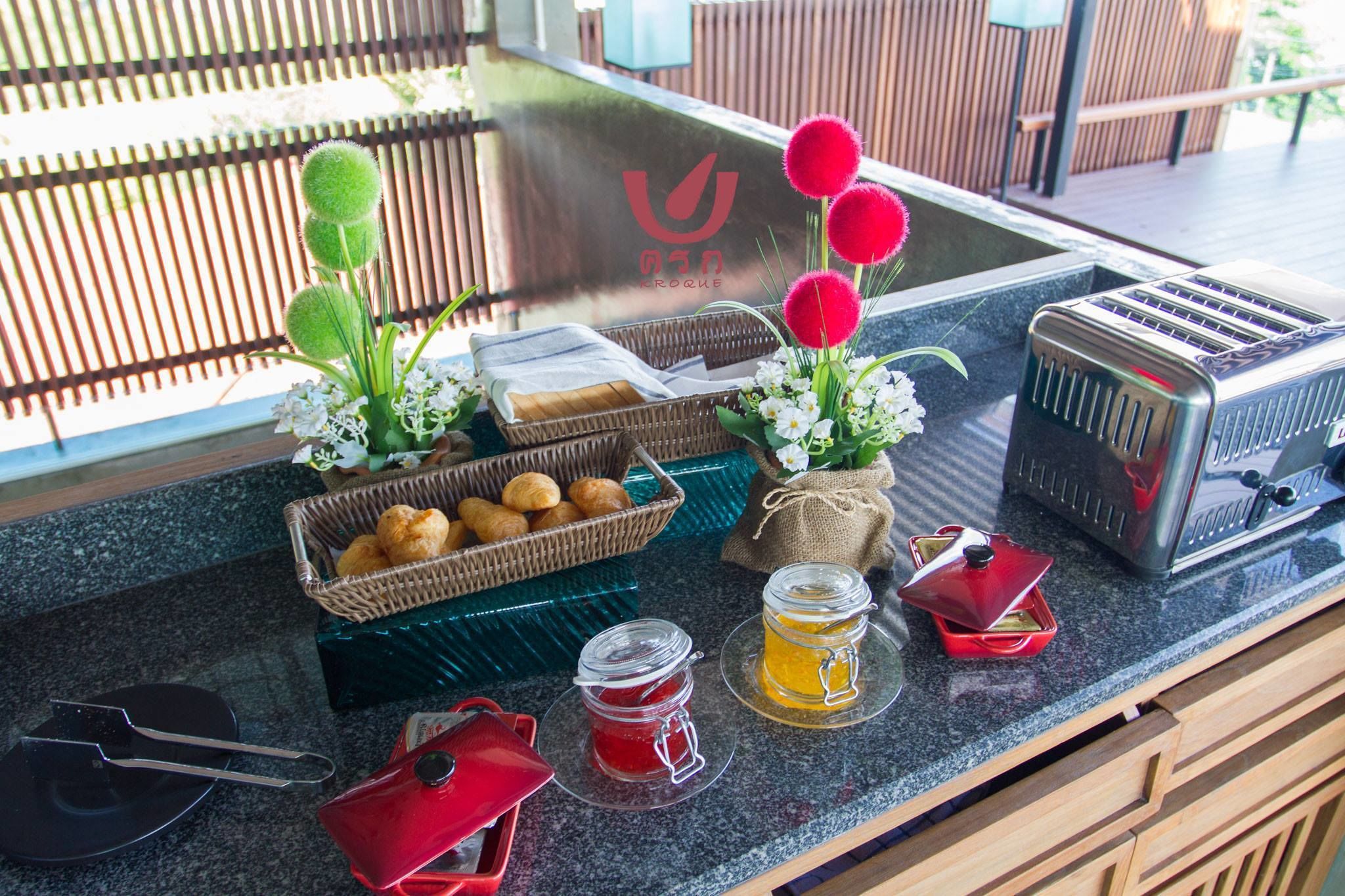 A breakfast setup with a toaster, croissants, a basket of pastries, a jar of jam, and a mug of tea on a granite countertop.